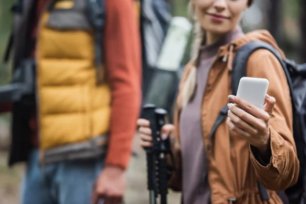 Abgeschnittene Ansicht einer lächelnden Frau, die ihr Smartphone in der Nähe ihres verschwommenen Freundes hält — Stockfoto