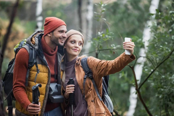Alegre pareja tomando selfie con senderismo palos en bosque — Stock Photo