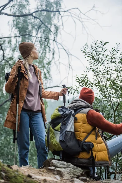 Paar mit Hut hält Wanderstöcke in der Hand, während es sich nach einer Wanderung im Wald ausruht — Stockfoto