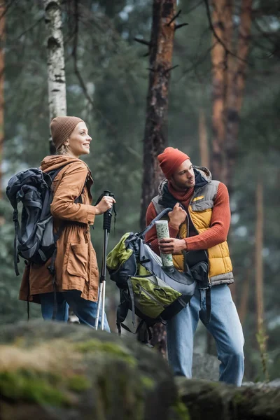 Homme tenant carte et sac à dos près femme gaie avec des bâtons de randonnée — Photo de stock