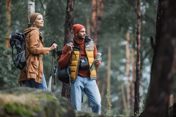 Uomo in possesso di mappa vicino donna allegra con bastoni da trekking — Foto stock