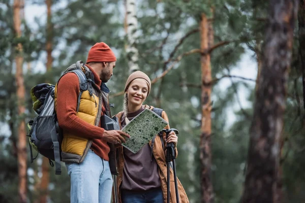 Man holding map and looking at cheerful woman with hiking sticks — Stock Photo