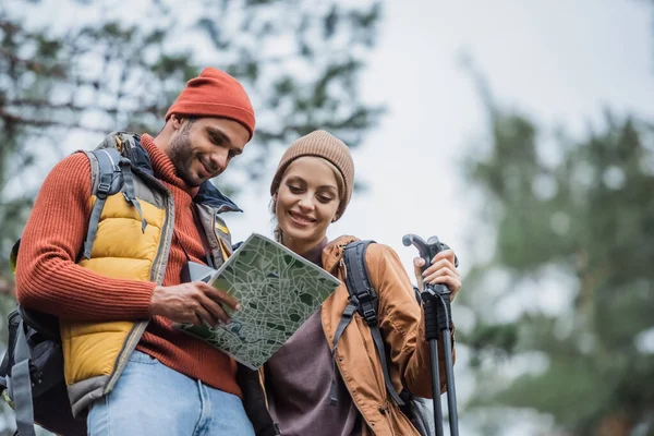 Vista de ángulo bajo de feliz pareja en sombreros mirando el mapa en el bosque - foto de stock