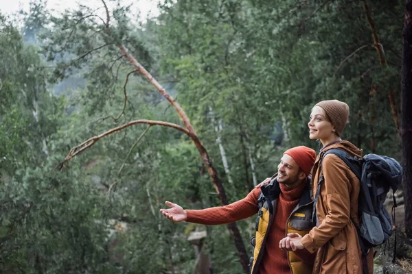 Man pointing with hand while holding hands with cheerful girlfriend in forest — Stock Photo