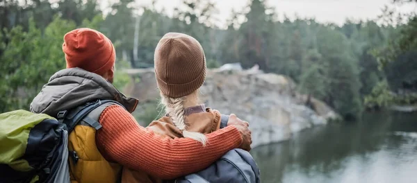 Вид ззаду чоловіка обіймає жінку біля озера, банер — стокове фото