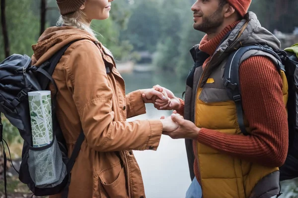 Vista recortada de pareja joven y alegre tomados de la mano cerca del lago en el bosque - foto de stock