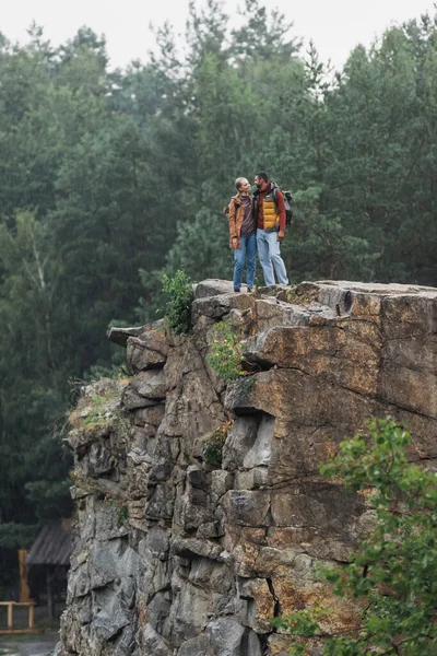 Casal alegre com caminhadas varas abraçando no penhasco rochoso — Fotografia de Stock