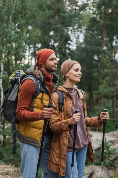 Pareja joven y complacida con mochilas trekking junto con bastones de senderismo - foto de stock