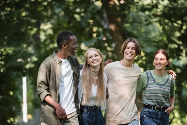 Alegres adolescentes multiétnicos abrazándose en el parque - foto de stock