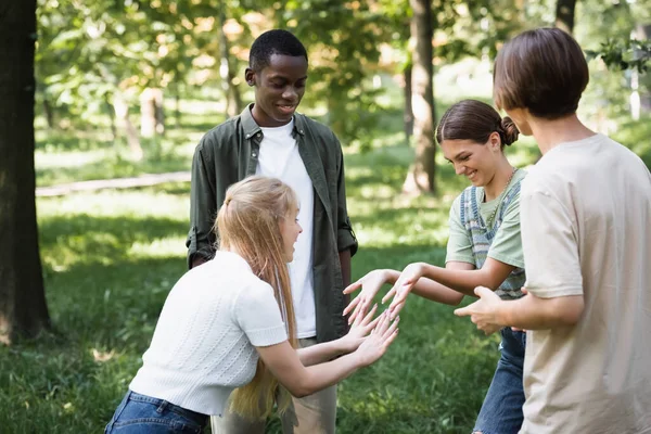 Sonrientes adolescentes jugando cerca de amigos multiétnicos en el parque - foto de stock