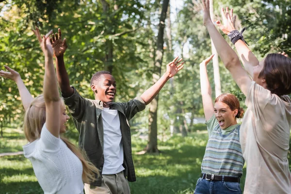 Emocionados adolescentes multiétnicos levantando las manos en el parque - foto de stock