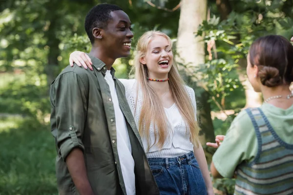 Sonriente adolescente chica abrazando africano americano amigo en parque - foto de stock