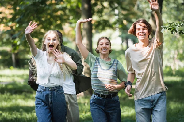 Happy interracial teenagers waving hands at camera in park — Stock Photo
