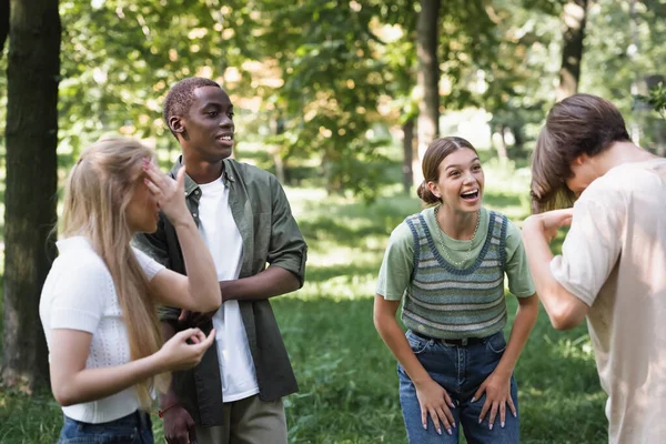 Lächelndes Mädchen schaut Freundin in der Nähe multiethnischer Teenager im Park an — Stockfoto