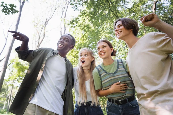Vista de bajo ángulo del niño afroamericano sonriente apuntando lejos cerca de amigos al aire libre — Stock Photo