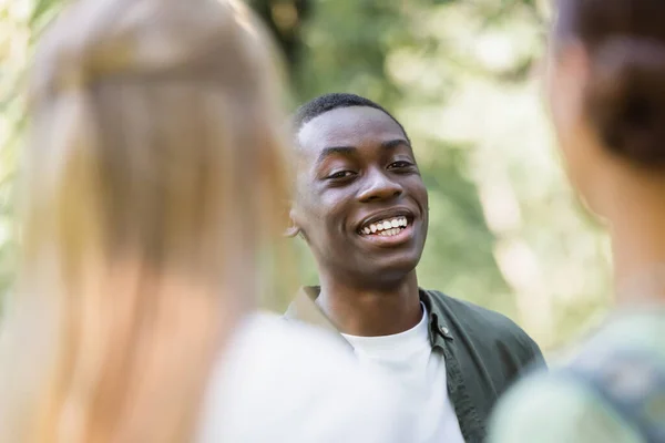 Улыбающийся африканский американский подросток смотрит в камеру рядом с размытыми друзьями — стоковое фото