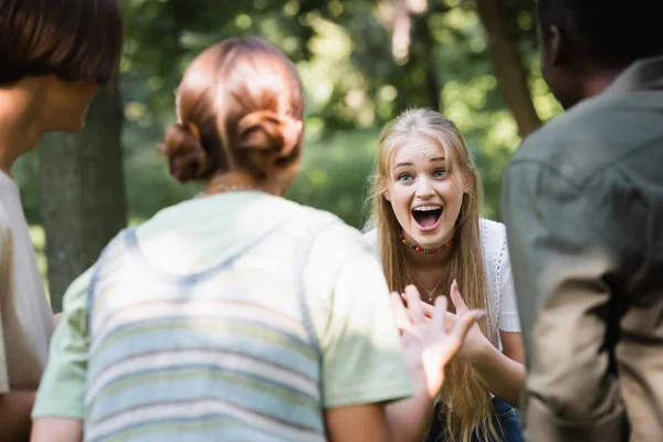 Excited teen girl looking at blurred interracial friends — Stock Photo