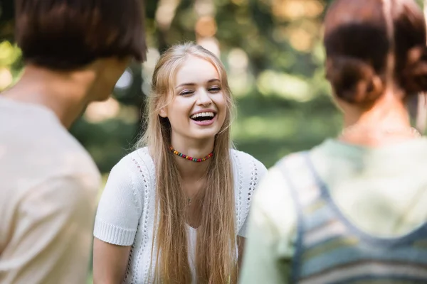 Cheerful teenager standing near blurred friends outdoors — Stock Photo