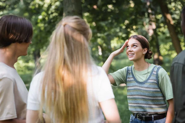 Smiling teenage girl standing near blurred interracial friends outdoors — Stock Photo