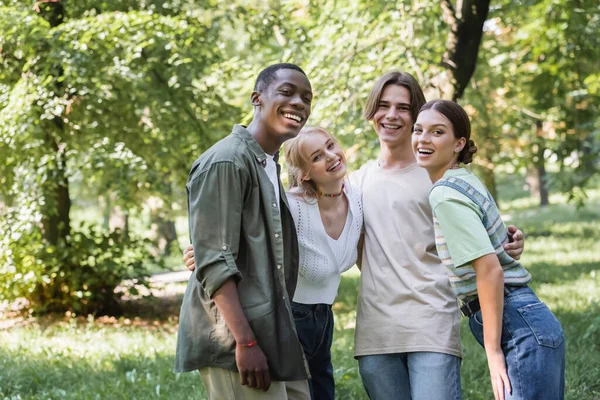 Adolescentes multiétnicos abrazando y mirando a la cámara en el parque - foto de stock