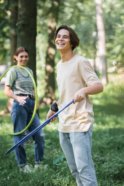 Positivo adolescente sosteniendo hula hoop cerca borrosa amigo - foto de stock