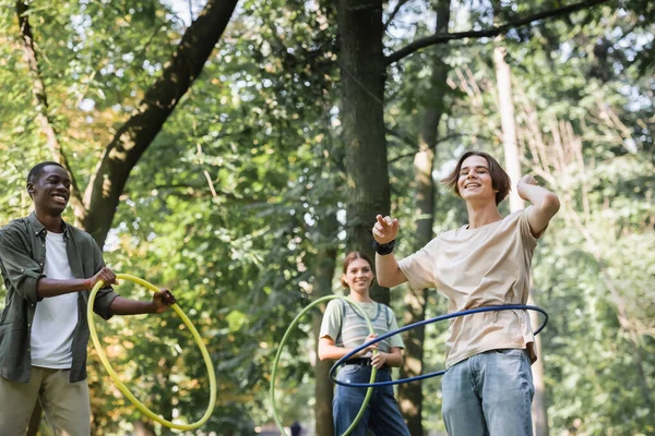 Tiefer Blickwinkel auf interrassische Teenager, die Hula-Hoop-Reifen im Park drehen — Stockfoto