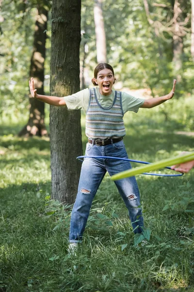 Emocionado adolescente torciendo hula hoop en la hierba en el parque - foto de stock
