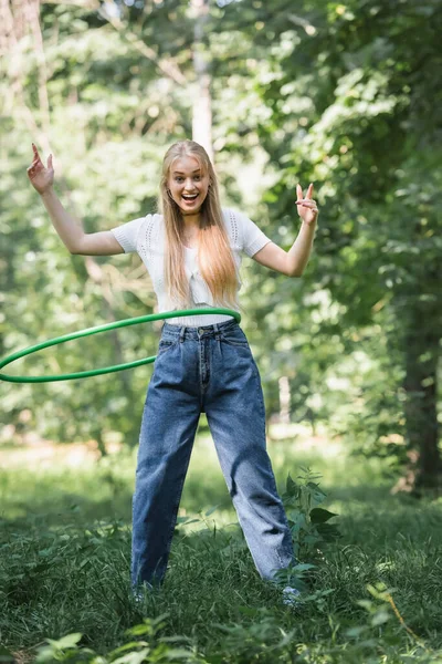 Sonriente adolescente torciendo hula hoop y mirando a la cámara en el parque - foto de stock