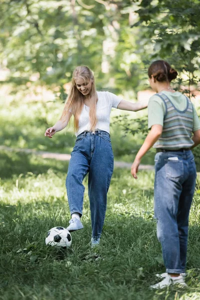 Menina adolescente jogando futebol com amigo desfocado no parque — Fotografia de Stock
