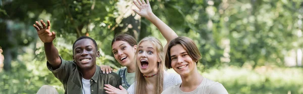Feliz interracial adolescentes agitando las manos en la cámara al aire libre, pancarta — Stock Photo