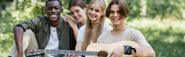 Feliz multiétnicos adolescentes sosteniendo la guitarra en el parque, pancarta - foto de stock