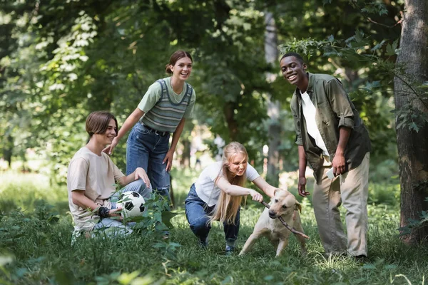 Sonrientes adolescentes multiétnicos jugando con palo y recuperador en el parque - foto de stock