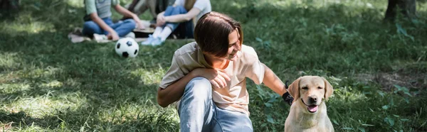 Souriant adolescent garçon caressant récupérateur près des amis flous dans le parc, bannière — Photo de stock