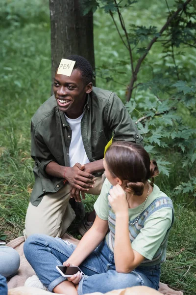 Vista aérea de adolescente afroamericano sonriente jugando quién soy con amigos en el parque - foto de stock