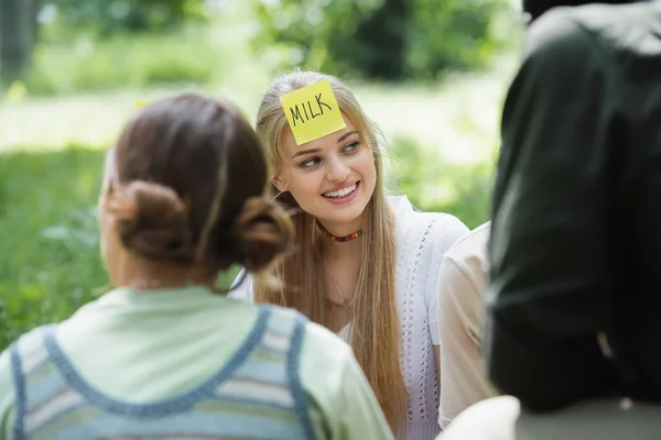 Adolescente sorridente con scritte di latte sull'adesivo che gioca chi sono con amici multietnici — Foto stock