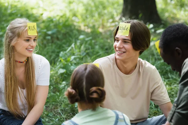 Adolescente alegre jugando quién soy juego con amigos multiétnicos - foto de stock