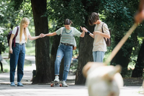 Adolescentes tomados de la mano de un amigo en el monopatín en el parque - foto de stock