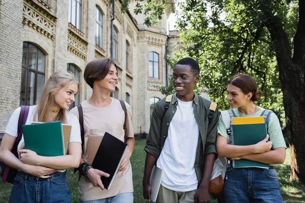 Lächelnde multiethnische Studenten mit Laptop und Notebooks im Freien — Stockfoto