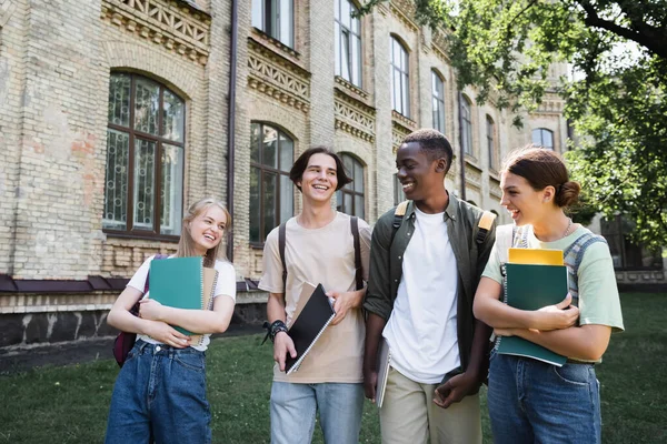 Positive multiethnic students with laptop and backpacks outdoors — Stock Photo