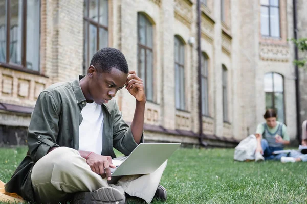 Зачарований афроамериканець дивиться на ноутбук на газоні. — стокове фото