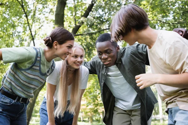 Adolescent afro-américain souriant embrassant des amis dans le parc — Photo de stock