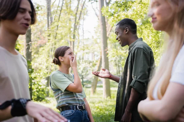 Adolescente afroamericano señalando a amigos alegres en el parque - foto de stock
