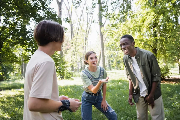 Adolescente sonriente señalando a un amigo afroamericano en el parque - foto de stock