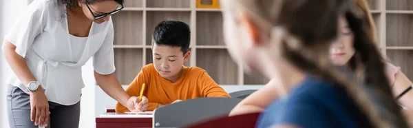 Africano americano profesor ayudar asiático escolar durante lección banner - foto de stock