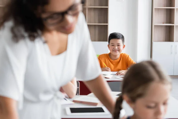 Selective focus of smiling asian schoolboy near african american teacher and girl on blurred foreground — Stock Photo