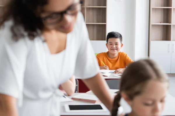 Selektiver Fokus lächelnder asiatischer Schüler in der Nähe afrikanisch-amerikanischer Lehrer und Mädchen auf verschwommenem Vordergrund — Stockfoto