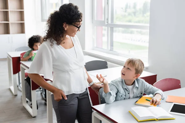 African american teacher standing with hand in pocket near boy gesturing while asking question — Stock Photo