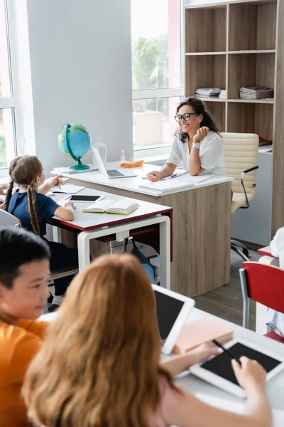 Blurred interracial pupils with digital tablets near smiling african american teacher — Stock Photo