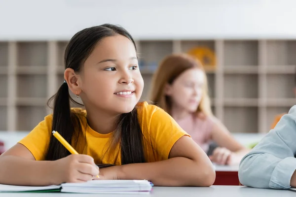 Счастливая девочка смотрит в сторону, держа ручку рядом с ноутбуком — стоковое фото