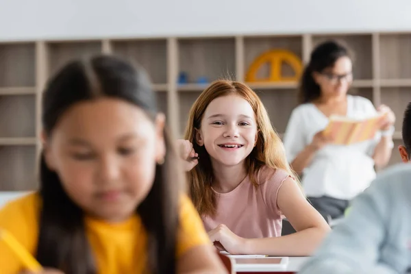 Вибірковий фокус рудої школярки, посміхаючись на камеру в класі — Stock Photo